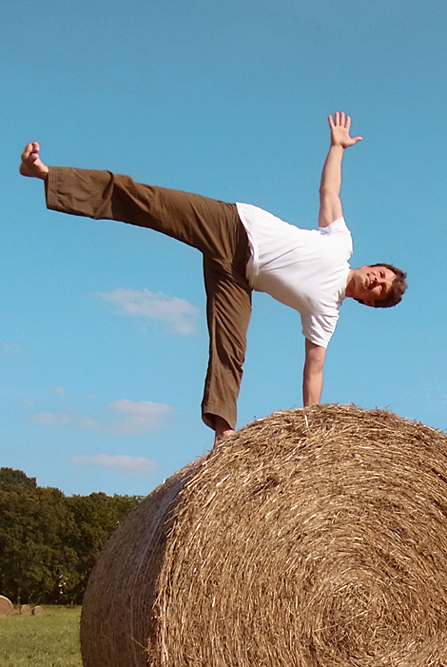 Yogalehrer Georg Hartmann in der Yogahaltung des Halbmondes auf einem Heuballen